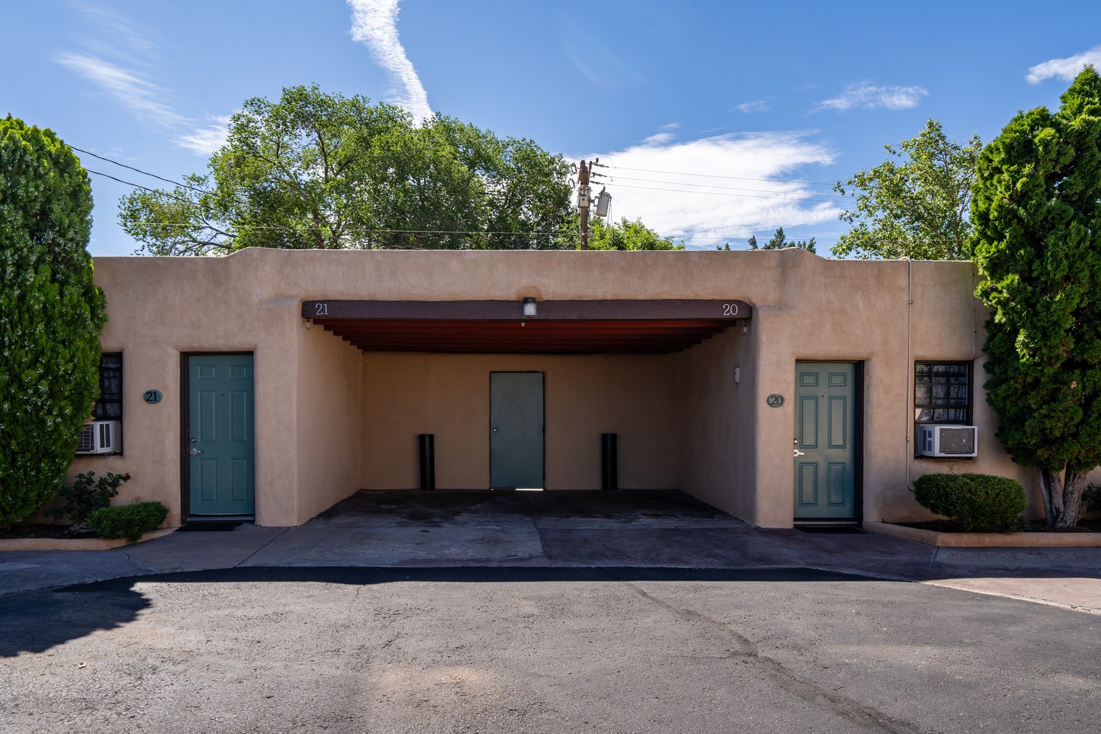 Covered carport between adobe rooms with green doors, parking right outside your room