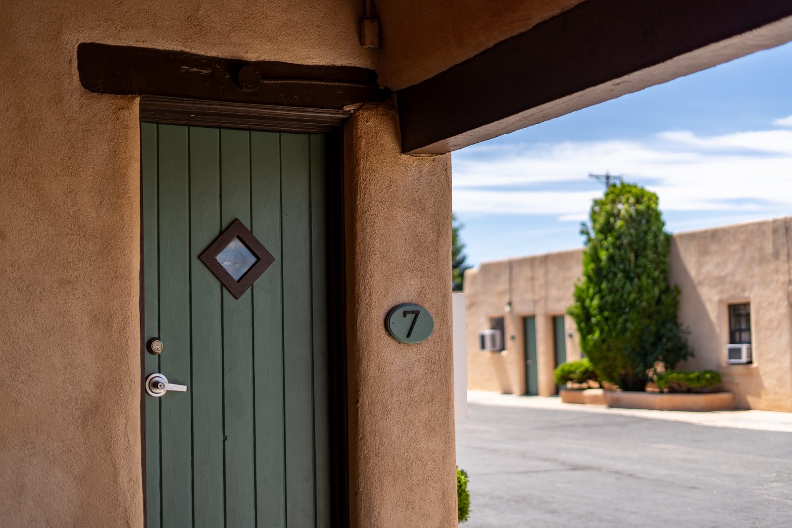 Green exterior door of room 7 under a carport beam, looking across the courtyard