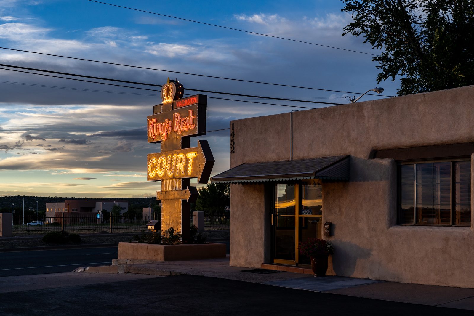 King's Rest Court neon sign glowing at dusk beside the adobe office on Cerrillos Road