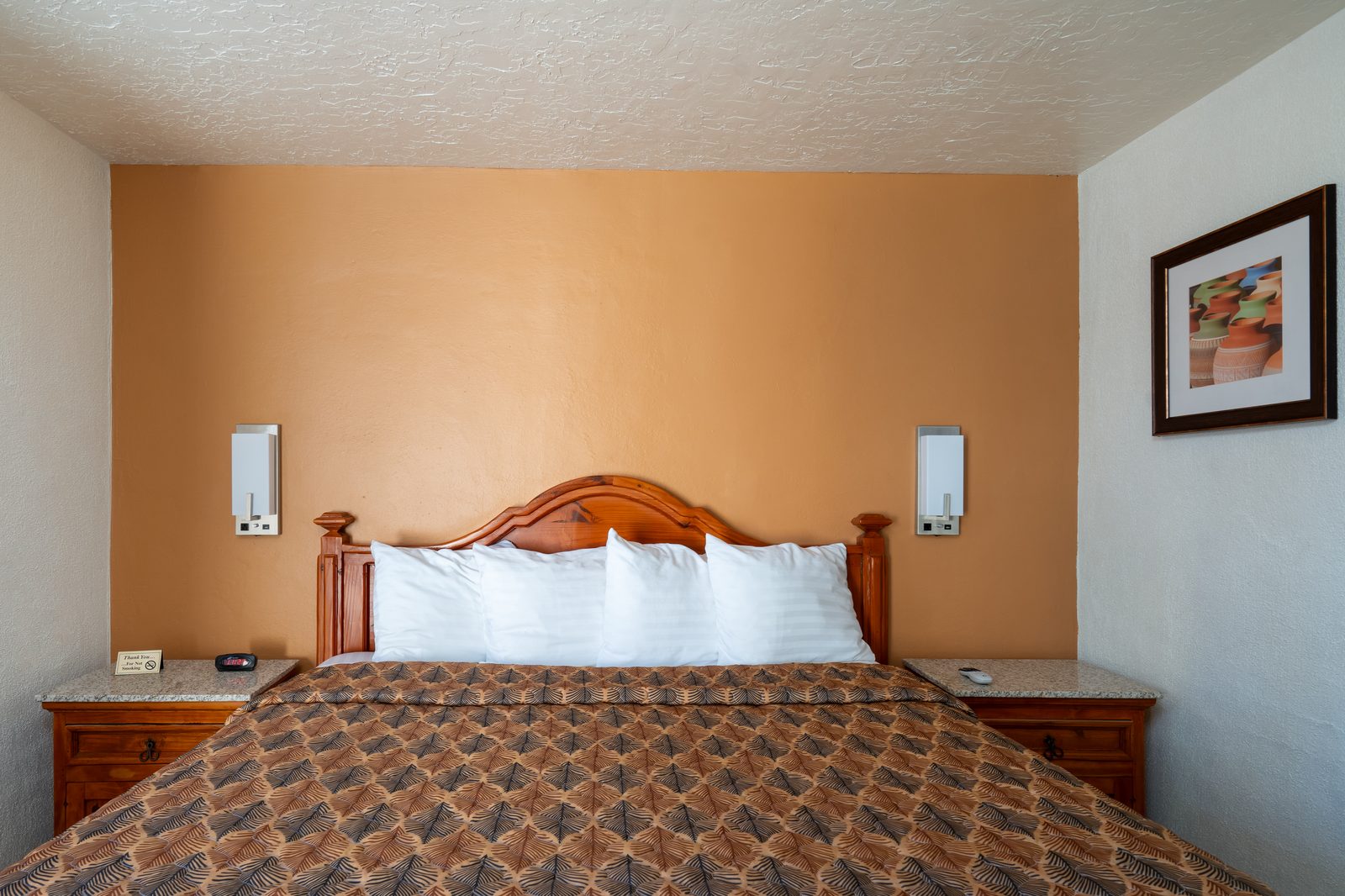King guest room with carved wood headboard, warm adobe-colored wall, and clean white pillows