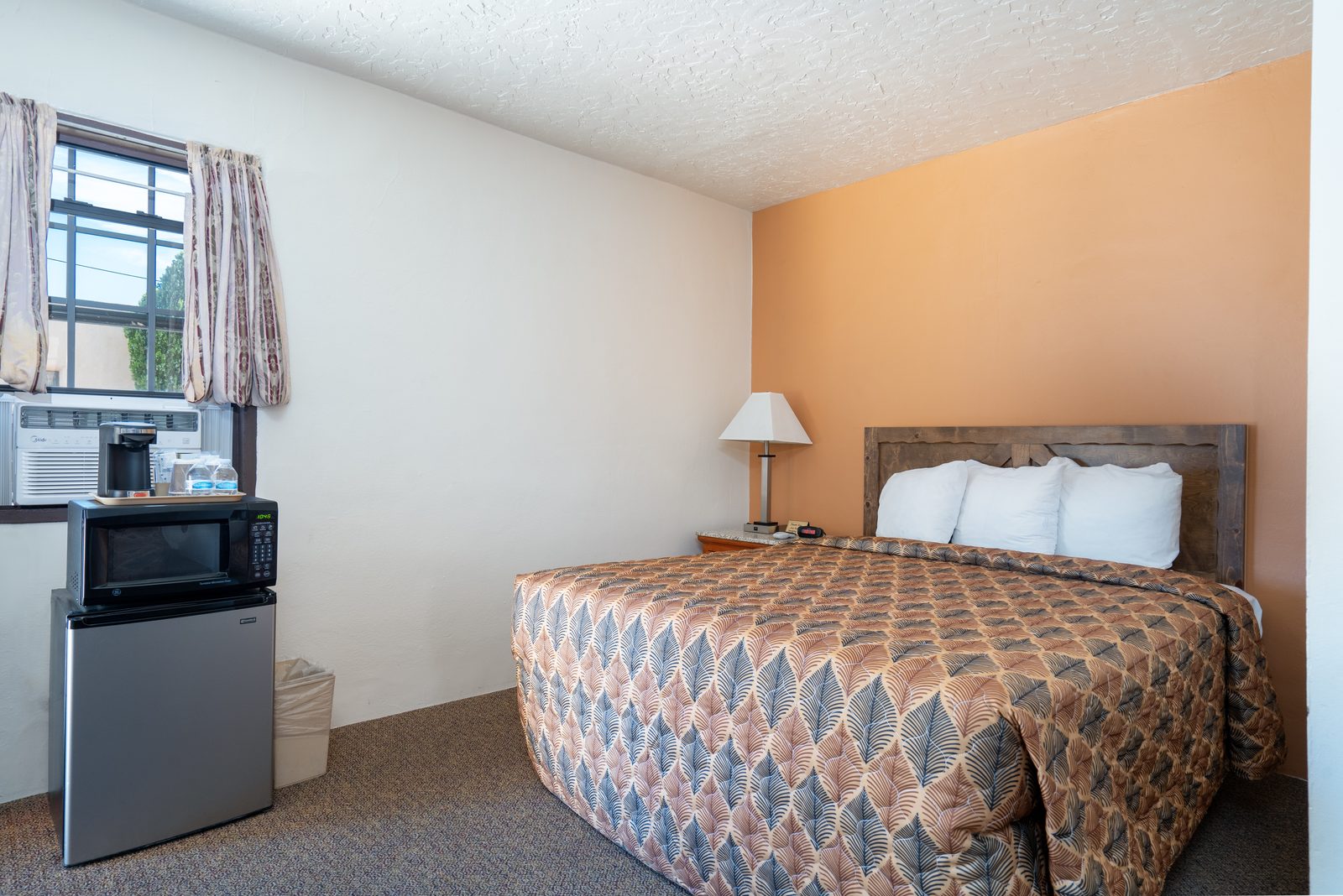 Queen guest room with fridge, microwave, coffee maker by the window, and a made bed